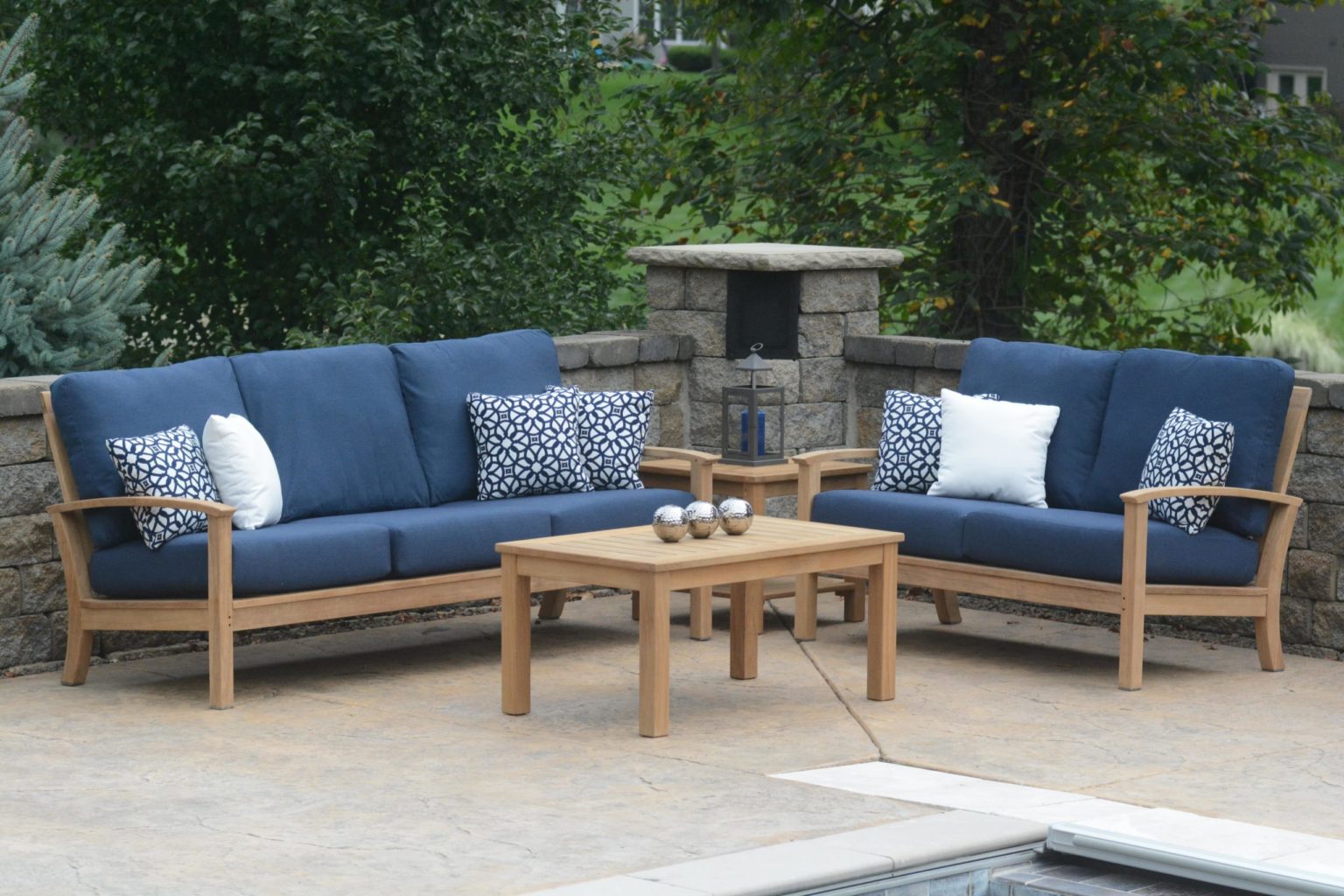 A St. Lucia outdoor patio furniture set including a two and three-seat sofa with navy cushions around a small table in the middle, all placed poolside