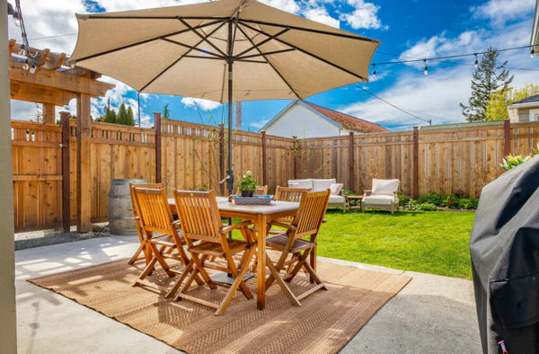A patio furniture set with a light coloured umbrella set up in a backyard