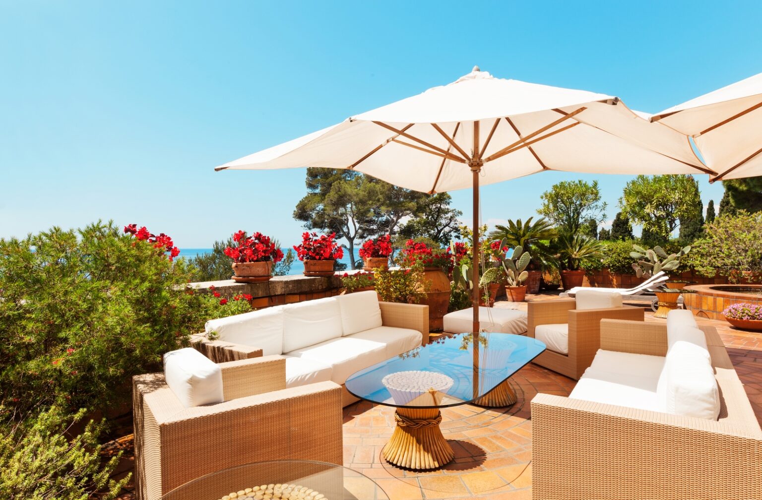 A white patio furniture set under the hot sun on a summer's day protected by a large white umbrella, surrounded by plants