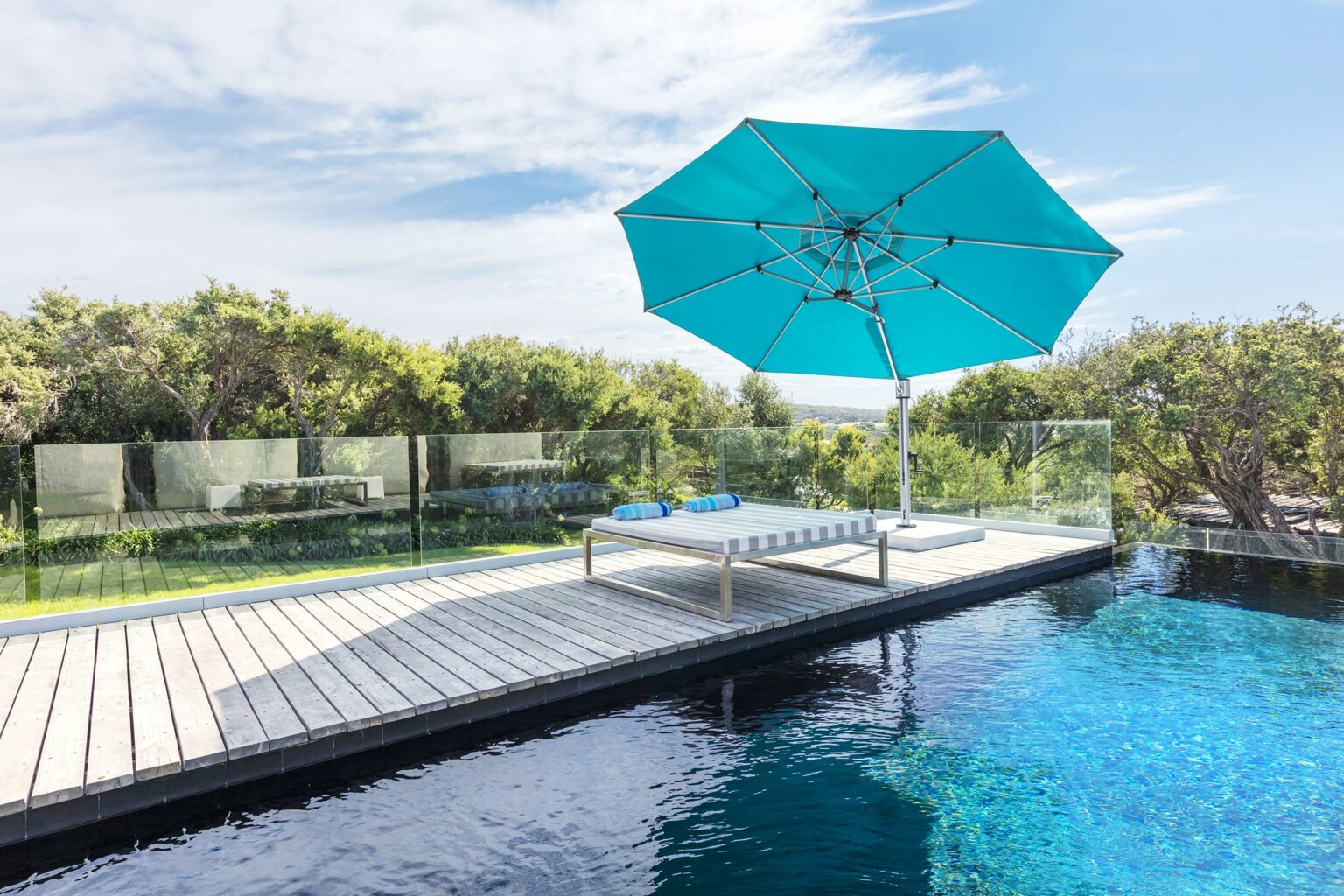 A light blue Eclipse 13' Octagon Cantilever Umbrella set up beside an outdoor pool on a warm summers day