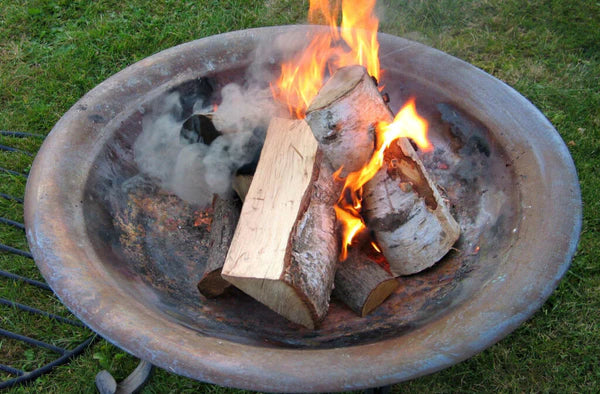 Close-up of a copper fire pit outdoors with burning wood.