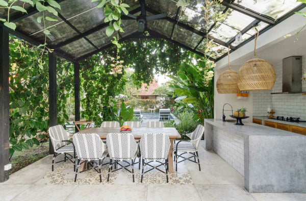 A modern open outdoor kitchen with dining tables and chairs in a garden setting.
