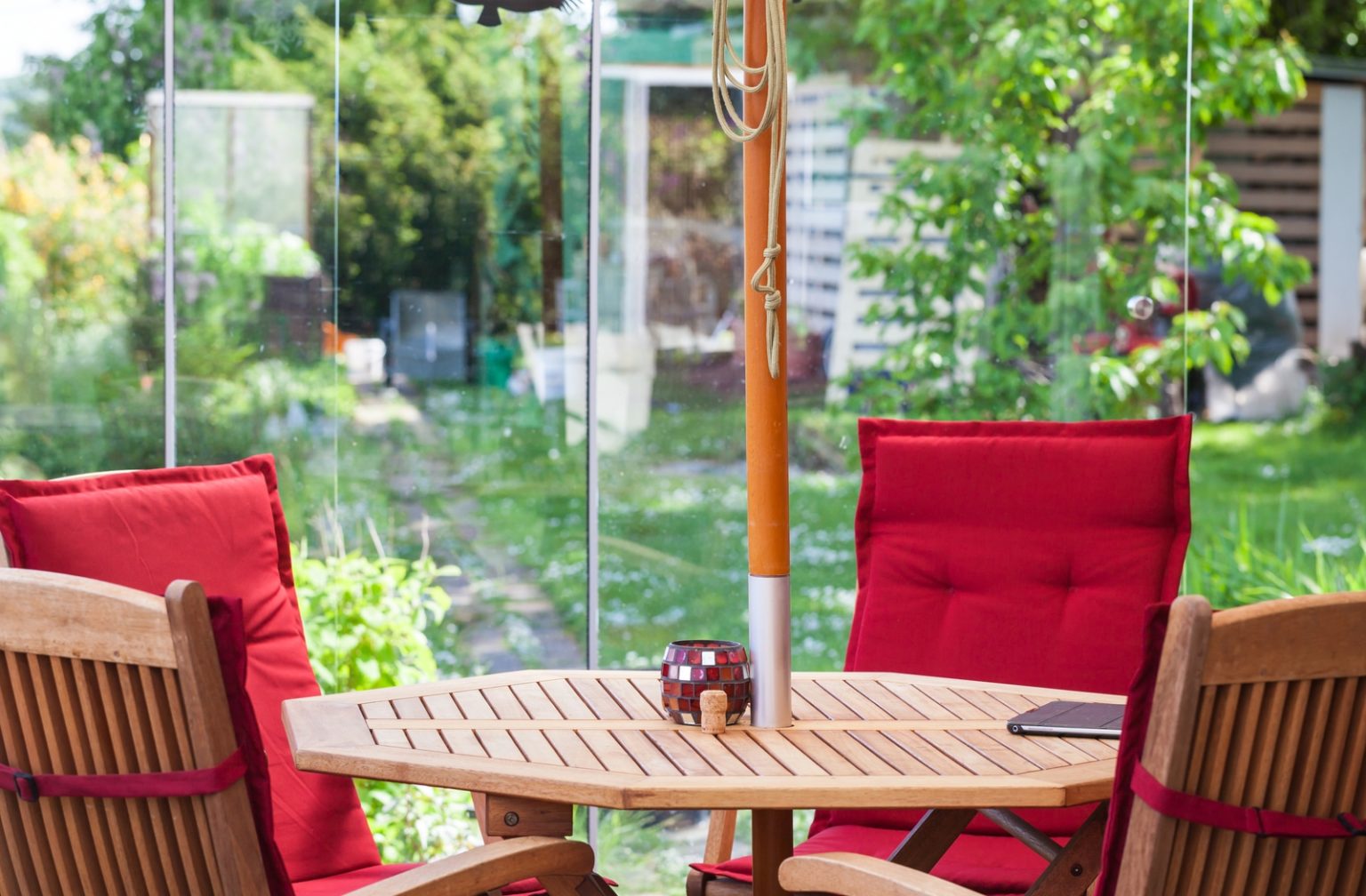 A teak outdoor patio furniture set with four chairs with bright red cushions surrounding a table